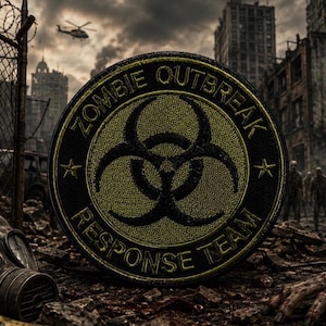 May include: A circular embroidered patch featuring a black biohazard symbol on a textured yellow background. The border is black with the yellow text ZOMBIE OUTBREAK RESPONSE TEAM and two small stars. The patch has a stitched edge finish.