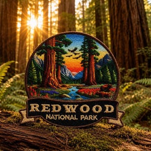 May include: Embroidered patch featuring a scenic view of Redwood National Park. The patch depicts tall redwood trees, a river, and a colorful sunset. The text "REDWOOD NATIONAL PARK" is displayed on a banner at the bottom.