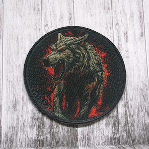 Może przedstawiać: Okrągła czarna łatka z białym wilkiem wyjącym z czerwonymi płomieniami za nim.
