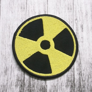 May include: A yellow and black embroidered patch with a radiation symbol. The symbol is a circle with three black blades inside.