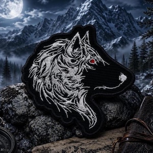 May include: An embroidered patch featuring a stylized white wolf head in profile against a black background. The wolf design includes intricate white thread detailing for fur and a single, small, vibrant red eye accent on a black fabric base.