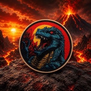 Puede incluir: Parche bordado redondo con un dinosaurio azul con ojos rojos y boca abierta, sobre un fondo rojo y amarillo. El parche tiene un borde dorado, con un volcán en llamas y una puesta de sol en el fondo.