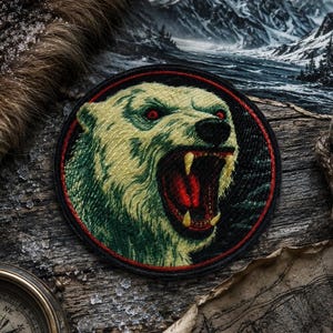 May include: A circular embroidered patch featuring a snarling polar bear with yellow fur, red eyes, and an open mouth showing sharp teeth. The bear is set against a dark background within a thin red border, creating a high-contrast graphic design.