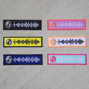 Op de afbeelding: Zes rechthoekige patches met een muzieknoot- en geluidsgolfontwerp. De patches zijn in verschillende kleuren: zwart, paars, geel, oranje, blauw en blauwgroen. Elke patch heeft een witte rand en een uniek kleurenschema.