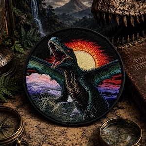 May include: Circular embroidered patch depicting a dinosaur with an open mouth against a sunset. The patch has a black border, and the dinosaur is in green and blue hues. The background shows a sun, water, and mountains. The patch is likely for clothing.