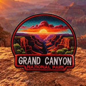 May include: Embroidered patch featuring a vibrant sunset over the Grand Canyon. The patch has a circular design with a red border and the words "GRAND CANYON NATIONAL PARK" in white lettering.