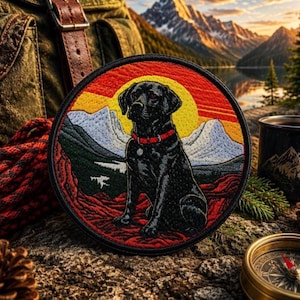 Puede incluir: Parche bordado redondo que representa un Labrador Retriever negro con un collar rojo, sobre un fondo de montañas y puesta de sol. El parche tiene un borde negro. El diseño evoca la aventura y las actividades al aire libre.