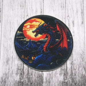 May include: A circular embroidered patch featuring a black dragon with red wings, perched on a mountaintop against a backdrop of a red moon and a dark blue sky.