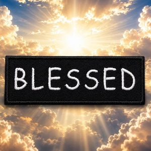 May include: A black rectangular patch with the word "BLESSED" embroidered in white. The patch is set against a background of a bright, sunny sky with fluffy white clouds and rays of light.