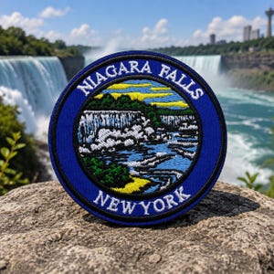 May include: A round, blue embroidered patch featuring a detailed depiction of Niagara Falls. The patch includes the text "NIAGARA FALLS" and "NEW YORK" in white lettering, with a central image of the falls in blue, white, green, and yellow.