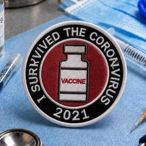 Puede incluir: Un parche bordado circular con un icono de vial de vacuna blanco y la palabra VACCINE en rojo. El borde negro tiene el texto blanco I SURVIVED THE CORONAVIRUS 2021 sobre un fondo circular de color rojo oscuro.