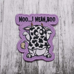 May include: Purple embroidered patch with a cow wearing a ghost costume. The text "Moo... I mean, Boo" is above the cow.