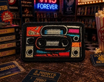May include: Embroidered patch featuring a retro cassette tape design with orange, blue, and pink accents. The patch is rectangular with a black border. The background includes VHS tapes, popcorn, and a neon sign that says "VHS FOREVER".