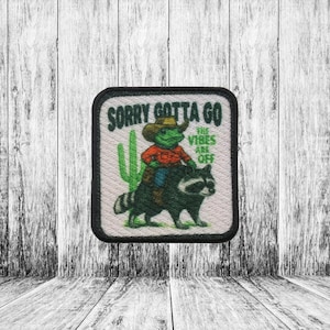 May include: Square patch with a black border. It features a cartoon frog in a cowboy hat and red shirt riding a raccoon. A green cactus is to the left. Text reads "SORRY GOTTA GO THE VIBES ARE OFF".