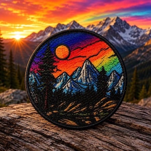May include: A circular embroidered patch featuring a vibrant sunset landscape with a bright orange sun, rainbow-coloured sky, snow-capped blue mountain peaks, and dark silhouettes of pine trees in the foreground, all enclosed by a black stitched border.