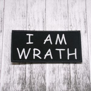 Puede incluir: Parche bordado negro con costuras blancas que dice "I AM WRATH".