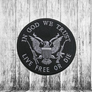 Op de afbeelding: Zwarte geborduurde patch met een witte adelaar en gekruiste geweren. De tekst "In God We Trust Live Free Or Die" is rond de adelaar geborduurd.