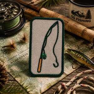 Peut inclure: Un écusson rectangulaire avec une bordure verte et une illustration d'une canne à pêche. L'écusson est posé sur une carte avec du matériel de pêche, dont un moulinet, des leurres et une tasse avec l'inscription "GO FISHING".