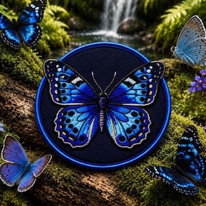 May include: A circular embroidered patch featuring a vibrant blue butterfly with black wing patterns and white accents. The patch has a dark blue border and is displayed against a background of mossy wood, small purple flowers, and several live butterflies.