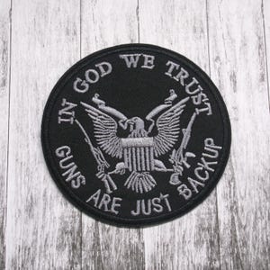 May include: Black and white embroidered patch with an eagle and guns. The text reads "In God We Trust Guns Are Just Backup".
