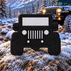 May include: A black embroidered patch shaped like the front view of an off-road vehicle. The design features a white rectangular windscreen, two circular headlights, a seven-slot vertical grille, and two smaller circular lights below the grille.