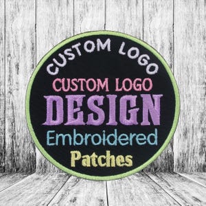 Op de afbeelding: Een ronde, zwarte geborduurde patch met een witte rand. De tekst op de patch luidt "Custom Logo Design Embroidered Patches" in verschillende kleuren.
