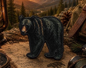 May include: Embroidered patch of a black bear in a walking pose. The patch has a detailed texture and is set against a backdrop of a map with "NATIONAL FOREST" printed on it. The bear patch is a camping or outdoor theme.