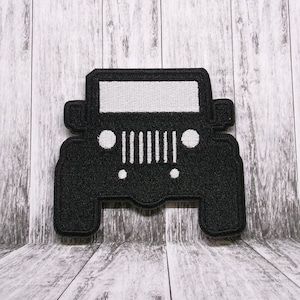 以下が含まれることがあります： 白いディテールが施されたジープの黒い刺繍パッチ。パッチには、白いグリル、ヘッドライト、白いフロントガラスがあります。