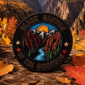 May include: A circular embroidered patch featuring a landscape of a blue river flowing through deep red canyons toward snow-capped mountains under a yellow sun. The black border displays the text BLACK CANYON OF THE GUNNISON with two stars.