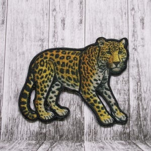 May include: A brown and black embroidered patch of a leopard with a yellow background.