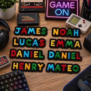 May include: A collection of eight embroidered name patches featuring the names James, Noah, Lucas, Emma, Daniel, Daniel, Henry, and Mateo in vibrant, multi-colored block letters with black outlines, arranged on a wooden surface with gaming accessories.