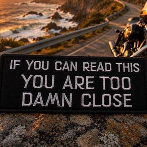 May include: A rectangular black embroidered patch with white stitched text that reads IF YOU CAN READ THIS YOU ARE TOO DAMN CLOSE. The patch features a clean border and bold, capitalized lettering designed for high visibility and clear communication.