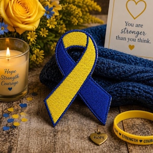 May include: A blue and yellow ribbon patch, a gold heart pendant with "HOPE" engraved, and a yellow bracelet with "HOPE STRENGTH COURAGE" text are displayed. A lit candle with "Hope Strength Courage" text and a card with "You are stronger than you think" text are also present.