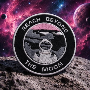 Könnte beinhalten: Runder, bestickter Aufnäher mit dem Text "REACH BEYOND THE MOON". Der Aufnäher zeigt einen Astronauten im Raumanzug, ein rosa-graues Design und einen schwarzen Rand. Der Hintergrund zeigt eine Galaxie mit Planeten.