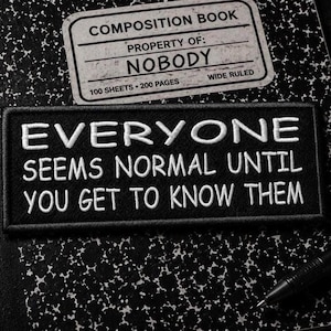 Puede incluir: Un parche rectangular negro bordado con texto blanco que dice: EVERYONE SEEMS NORMAL UNTIL YOU GET TO KNOW THEM. El parche está colocado sobre un cuaderno de composición con manchas blancas y negras y una etiqueta que dice PROPERTY OF: NOBODY.