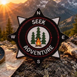 May include: A black, star-shaped embroidered patch featuring a white center with three green pine trees and a small orange campfire. The text SEEK ADVENTURE is stitched in white, with N, S, E, and W compass points at the star tips and red accents.