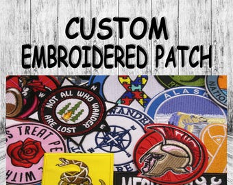 Könnte beinhalten: Eine Sammlung bunter gestickter Patches mit verschiedenen Designs, darunter ein Kompass, eine Schlange, eine Rose, ein Mechaniker-Symbol und eine Wildnis-Szene. Die Patches sind auf einem Holzgrund mit dem Text "CUSTOM EMBROIDERED PATCH" oben angeordnet.
