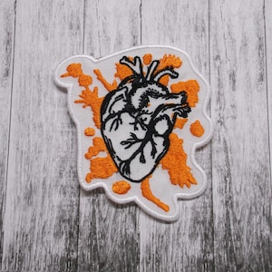 May include: White embroidered patch with a black anatomical heart design surrounded by orange splatter paint.