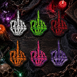May include: Six embroidered patches shaped like skeletal hands making a middle finger gesture. The patches are colored white, lime green, red, orange, hot pink, and purple, each featuring black outlines and detailed bone structures on a dark background.