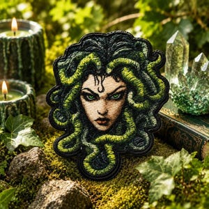 Puede incluir: Parche bordado con una detallada ilustración de Medusa con cabello verde de serpiente y penetrantes ojos verdes. El parche tiene un borde negro y está sobre un fondo musgoso con velas y cristales.