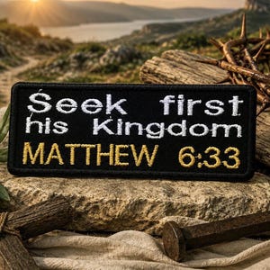 May include: Black rectangular patch embroidered with the words "Seek first his Kingdom MATTHEW 6:33" in white and gold thread. The patch is set against a natural backdrop with a crown of thorns and a cross.