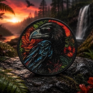 Puede incluir: Parche bordado circular con un diseño de cuervo. El cuervo negro tiene detalles azules y rojos, rodeado de flores y follaje. El parche tiene un borde negro, adecuado para chaquetas, bolsos u otros artículos de tela.