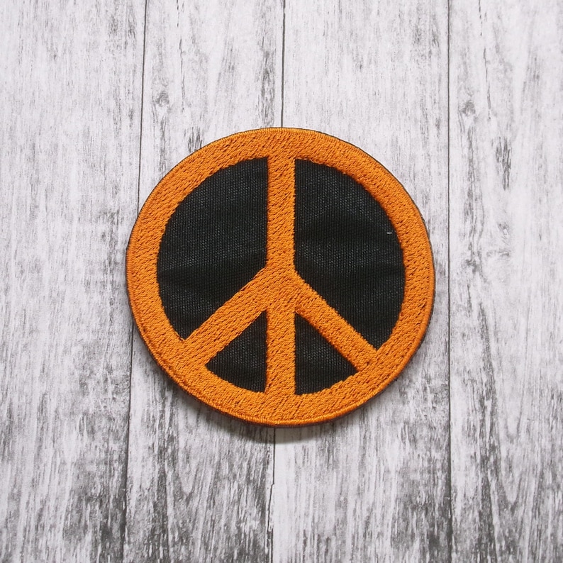 May include: Orange peace sign embroidered patch on a white wood background.