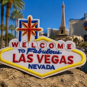 Könnte beinhalten: Ein weißer gestickter Aufnäher in Form des ikonischen Welcome to Fabulous Las Vegas Schildes. Der Aufnäher zeigt rote Schriftzüge mit dem Text Welcome to Fabulous Las Vegas Nevada, einen gelben Rand und ein rotes Sternsymbol oben.