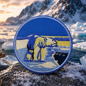 Könnte beinhalten: Ein kreisförmiger bestickter Aufnäher mit einem Eisbären, der auf einer verschneiten Landschaft steht. Der Bär ist in Gelb- und Weißtönen vor einem leuchtend blauen Hintergrund dargestellt. Der Aufnäher hat einen gestickten Rand in Hellblau.