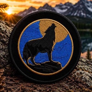 May include: A circular embroidered patch featuring a black wolf silhouette howling at a large golden moon set against a vibrant blue background. The design is enclosed within a thin golden border and a thick black outer edge, creating a distinct emblem.