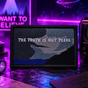 May include: A rectangular patch with the text "THE TRUTH IS OUT THERE" in white. The patch features a blue and gray design with a black border. The background includes a neon sign that says "I WANT TO BELIEVE".