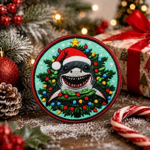 May include: A round patch featuring a shark wearing a Santa hat and surrounded by a Christmas tree. The shark has a wide grin, and the tree is decorated with colorful lights and a gold star. The patch has a red border.