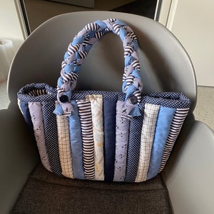 Peut inclure: Un sac cabas en patchwork bleu et blanc avec une anse en tissu tress&eacute;e. Le sac est fait de diff&eacute;rents tissus &agrave; rayures, &agrave; pois et &agrave; carreaux.