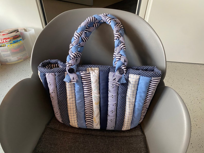 Peut inclure: Un sac cabas en patchwork bleu et blanc avec une anse en tissu tress&eacute;e. Le sac est fait de diff&eacute;rents tissus &agrave; rayures, &agrave; pois et &agrave; carreaux.